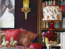 Aurora lamp in red glaze with 23k gold base, brass double socket cluster, and a custom floral lampshade, installed on an end table in a decorated living room.