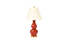 Small Alexander lamp in raspberry glaze with a 23k gold water gilt base, brass double socket cluster, and off white vellum paper shade, on a white background.