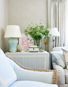 A Single Douglas Table Lamp with Hand Slip Trailed Chevron Detail in Duck Egg Glaze with 23k gold water gilt base, brass double socket cluster, and off white vellum paper lamp shade, installed on an end table next to a sofa in a living room decorated by Mark Sikes.
