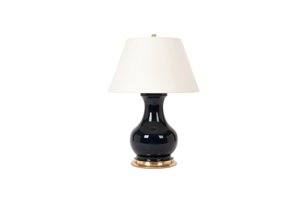 A single Medium Hann table lamp in navy glaze with a 23k gold base, brass double socket cluster, and off white vellum paper shade, on a white background.