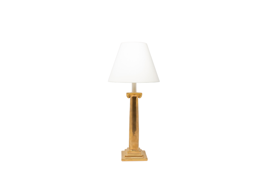 Ionic candlestick lamp in gold luster glaze with an off white vellum paper lampshade, on a white background.